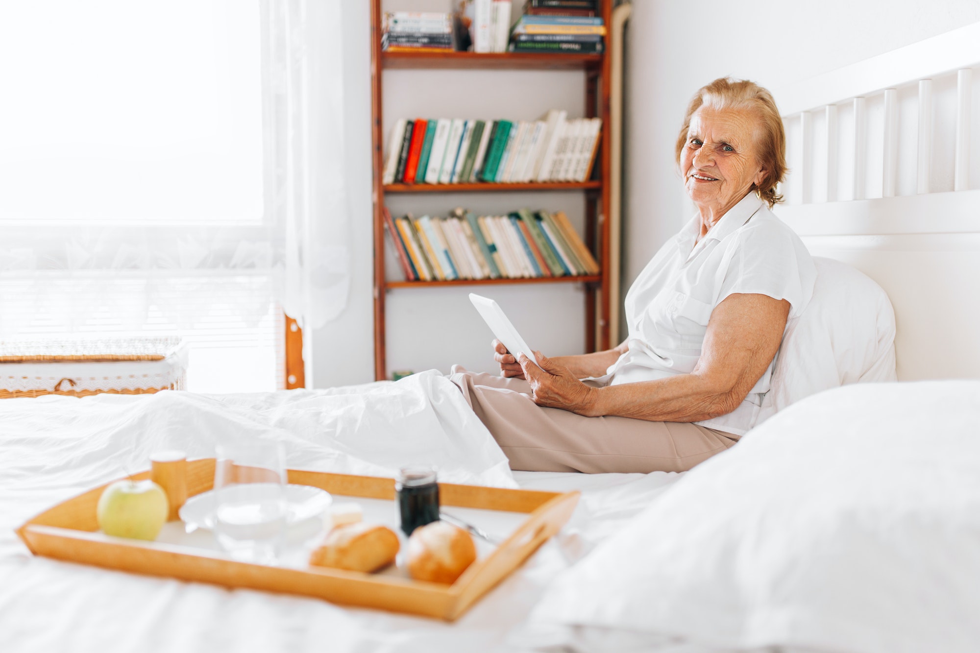 Elderly woman having breakfast in bed whilst using her tablet